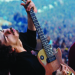 Young Carlos Santana on outdoor stage playing guitar