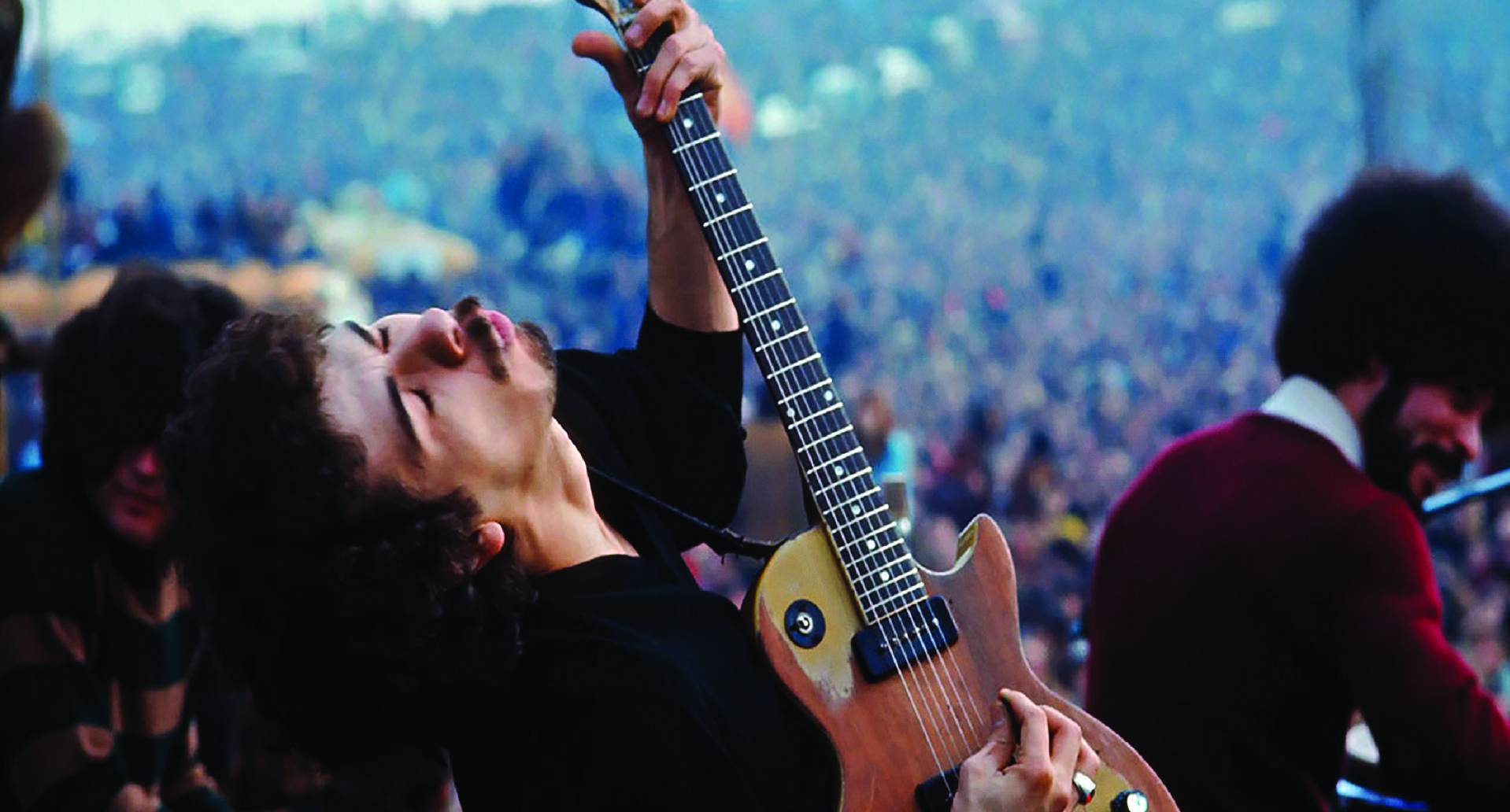 Young Carlos Santana on outdoor stage playing guitar